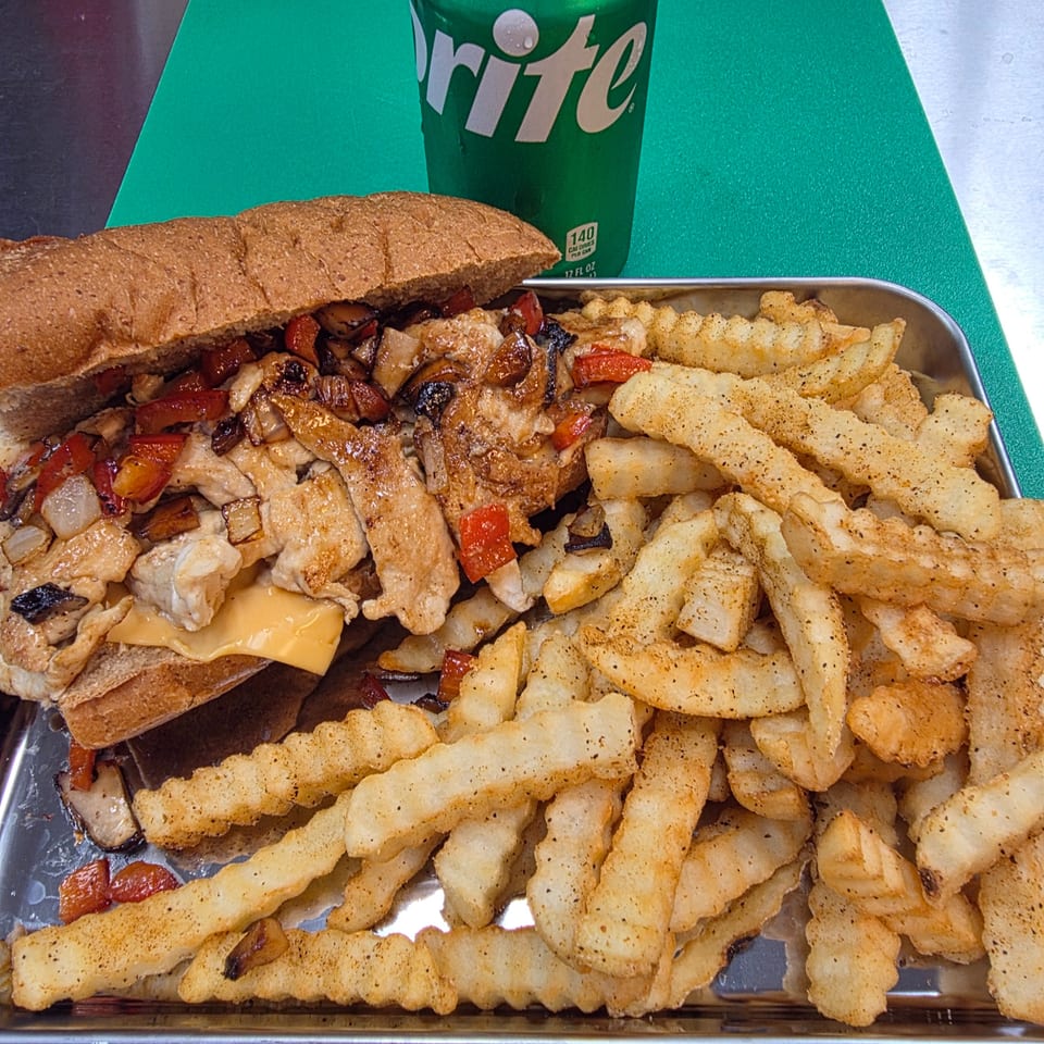 Chicken cheesesteak with peppers, onions, and mushrooms, served with crinkle-cut fries and a Sprite.