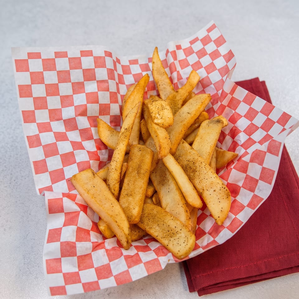 Seasoned steak fries in a red and white checkered paper basket, resting on a red napkin.